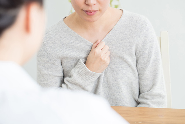 服の胸もとをそっと持って診察を受ける女性